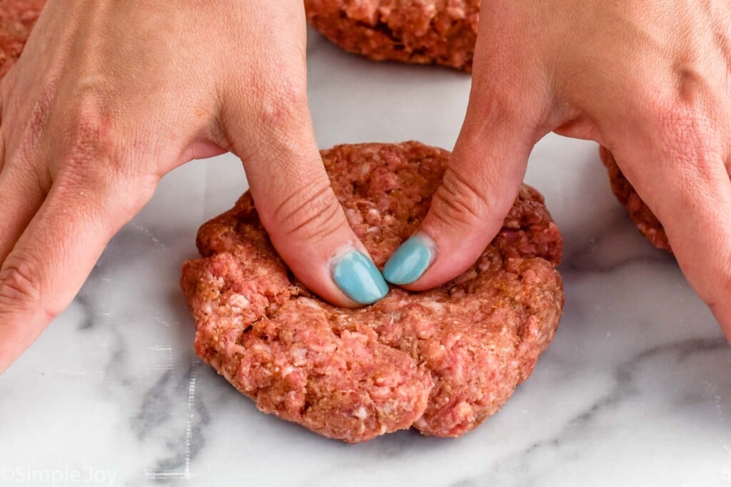 person's fingers pushing into the center of a hamburger patty to show how to make hamburgers