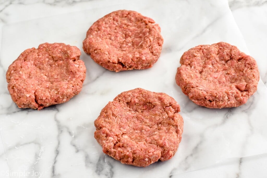 Four hamburger patties on a piece of parchment paper