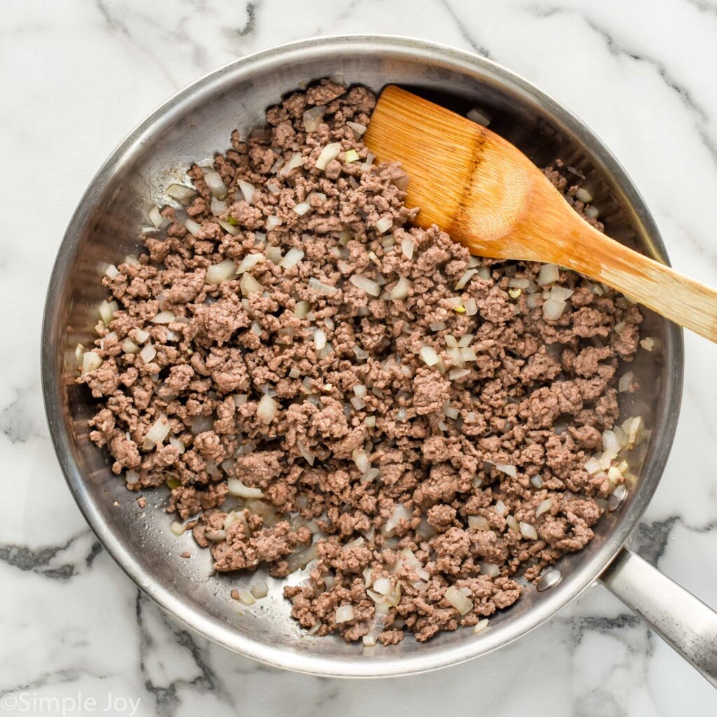 Overhead of skillet of ground beef and diced onion with wooden spoon to make Walking Tacos