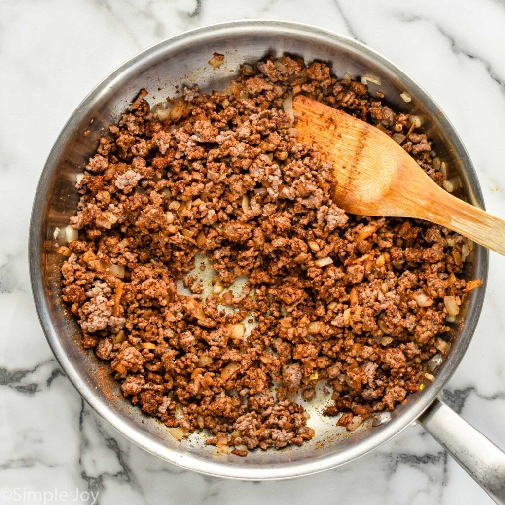 overhead of skillet of ground beef, diced onions, and taco seasoning to make Walking Tacos with wooden spoon