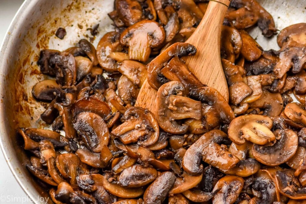 overhead of skillet of sauteed mushrooms with wooden spoon.