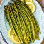 overhead view of oven roasted asparagus with lemon slices on a blue platter