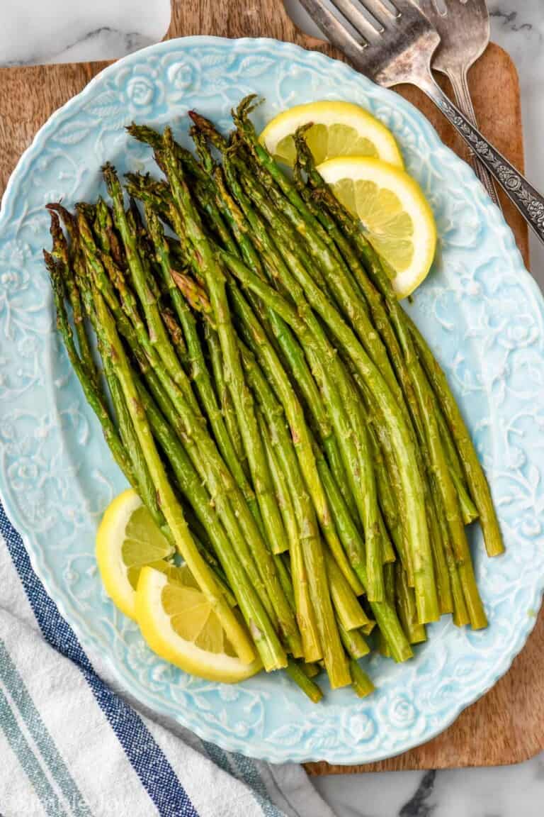overhead view of oven roasted asparagus with lemon slices on a blue platter