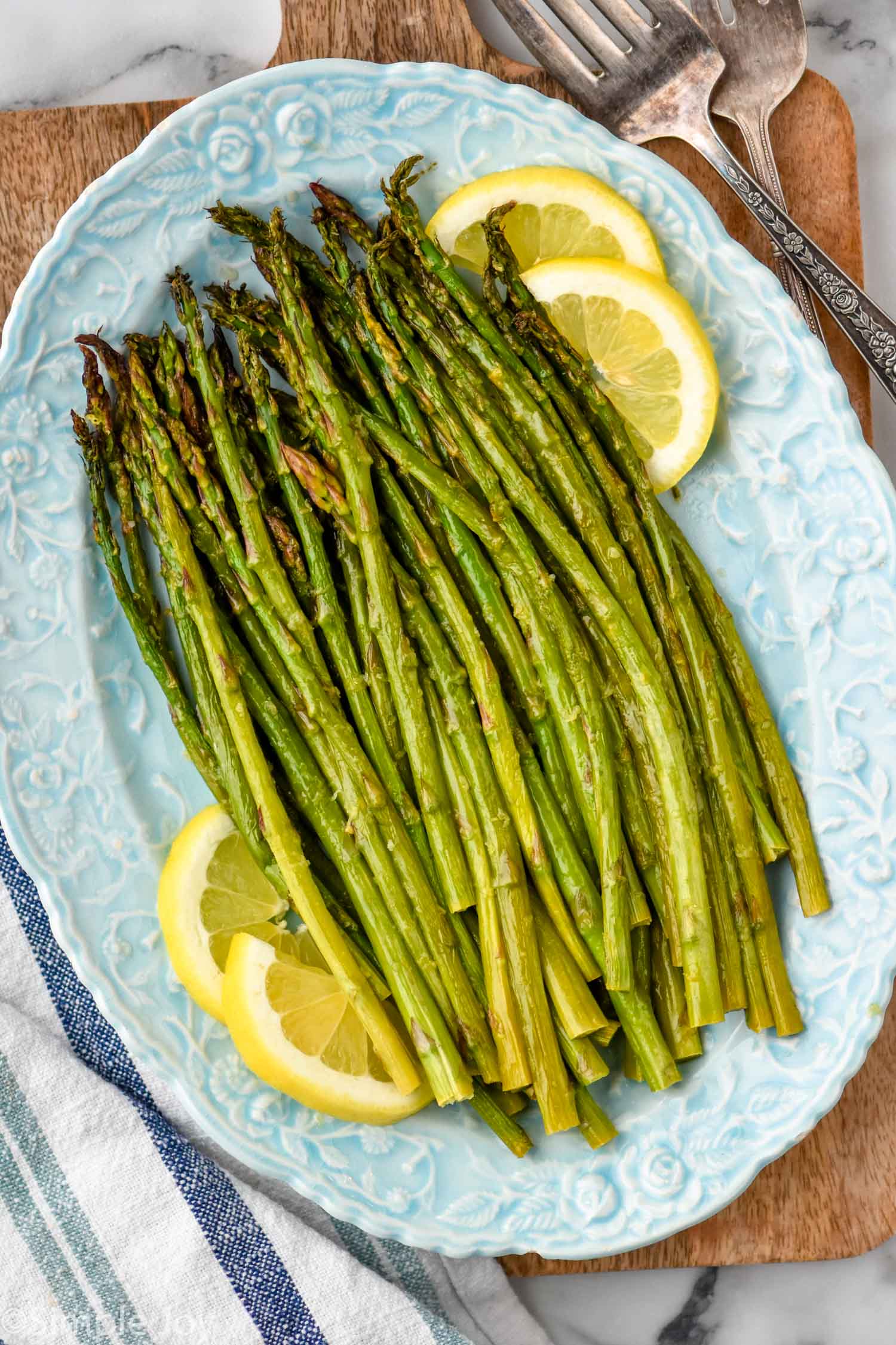 overhead view of oven roasted asparagus with lemon slices on a blue platter