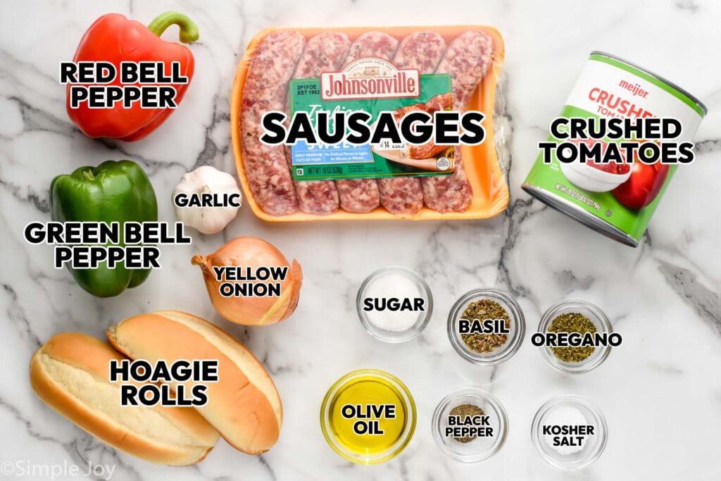 overhead of ingredients for sausage and peppers, labeled: red and green bell peppers, hoagie rolls, yellow onion, garlic, sausages, crushed tomatoes, sugar, basil, oregano, olive oil, black pepper, kosher salt