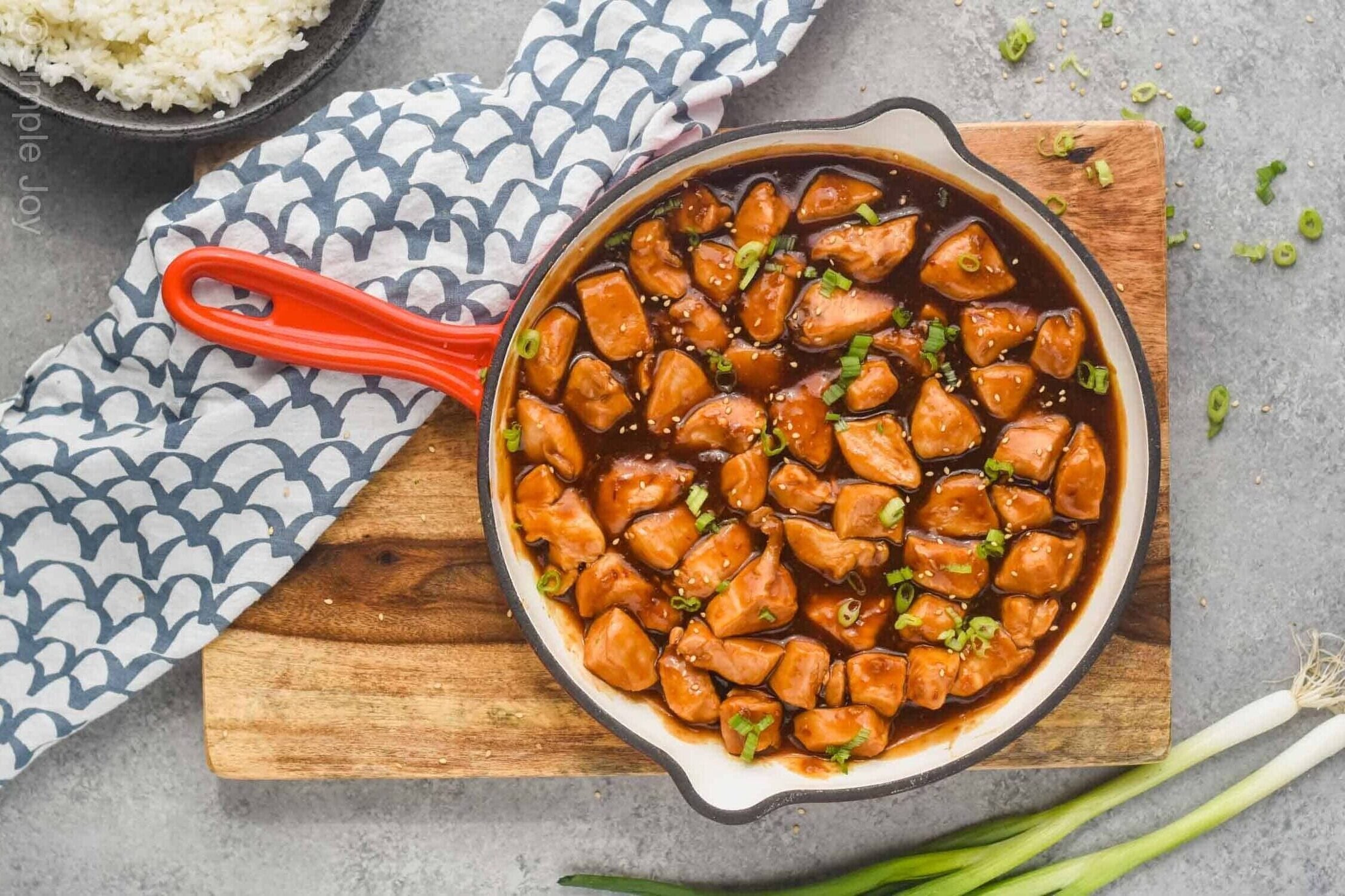 overhead view of a skillet holding sticky chicken recipe garnished with sesame seeds and sliced green onion - 3