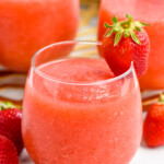 Glass of Strawberry Daiquiri with a strawberry on the rim. Two glasses of Strawberry Daiquiri and fresh strawberries sitting behind