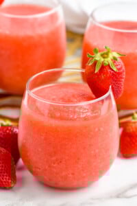 Glass of Strawberry Daiquiri with a strawberry on the rim. Two glasses of Strawberry Daiquiri and fresh strawberries sitting behind