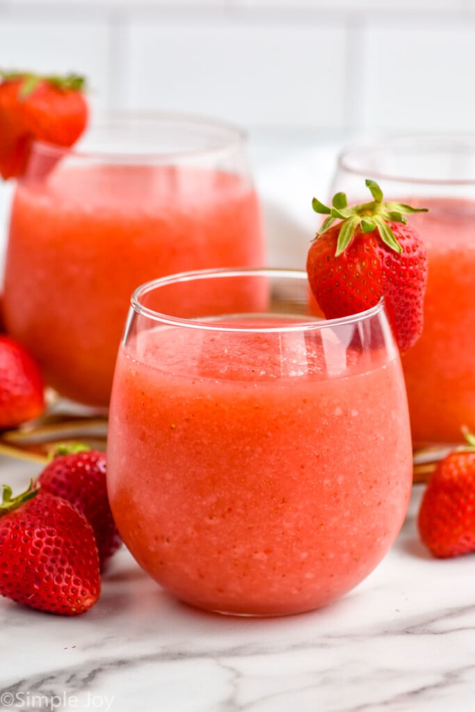 Glass of Strawberry Daiquiri with a strawberry on the rim. Two glasses of Strawberry Daiquiri and fresh strawberries sitting behind