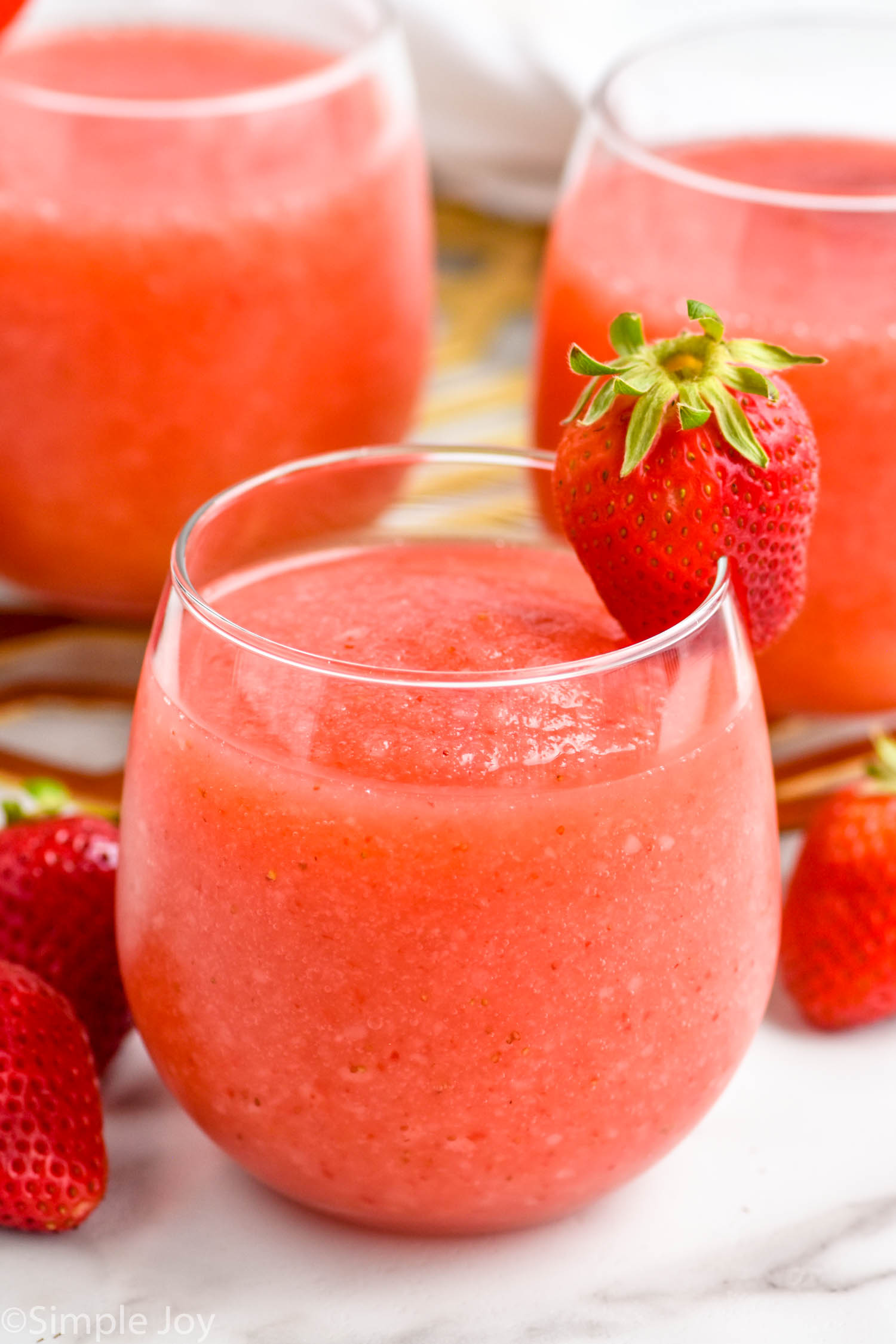 Glass of Strawberry Daiquiri with a strawberry on the rim. Two glasses of Strawberry Daiquiri and fresh strawberries sitting behind