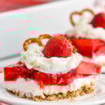 Piece of Strawberry Pretzel Salad topped with whipped cream, strawberry, and a pretzel