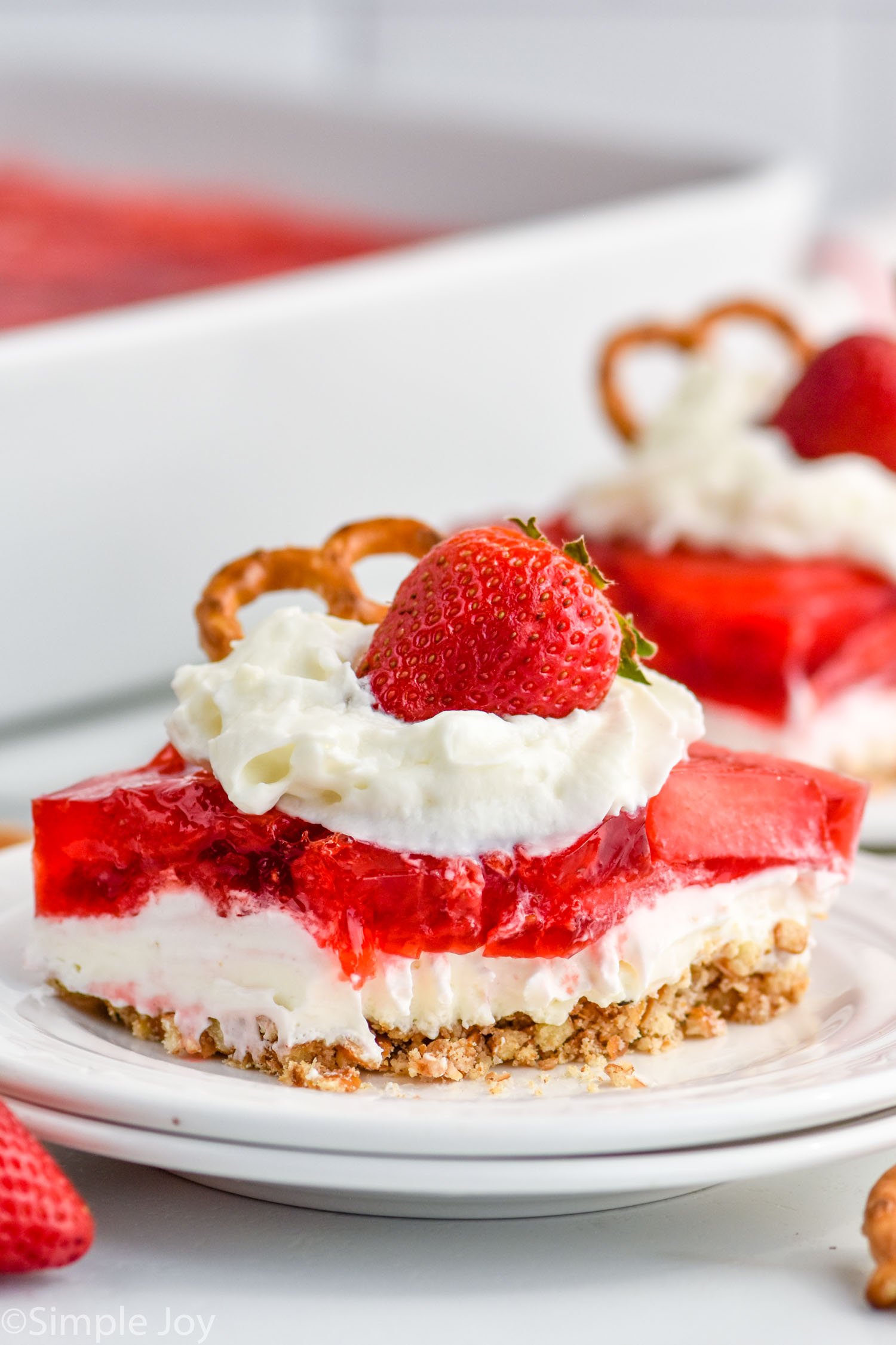 Piece of Strawberry Pretzel Salad topped with whipped cream, strawberry, and a pretzel