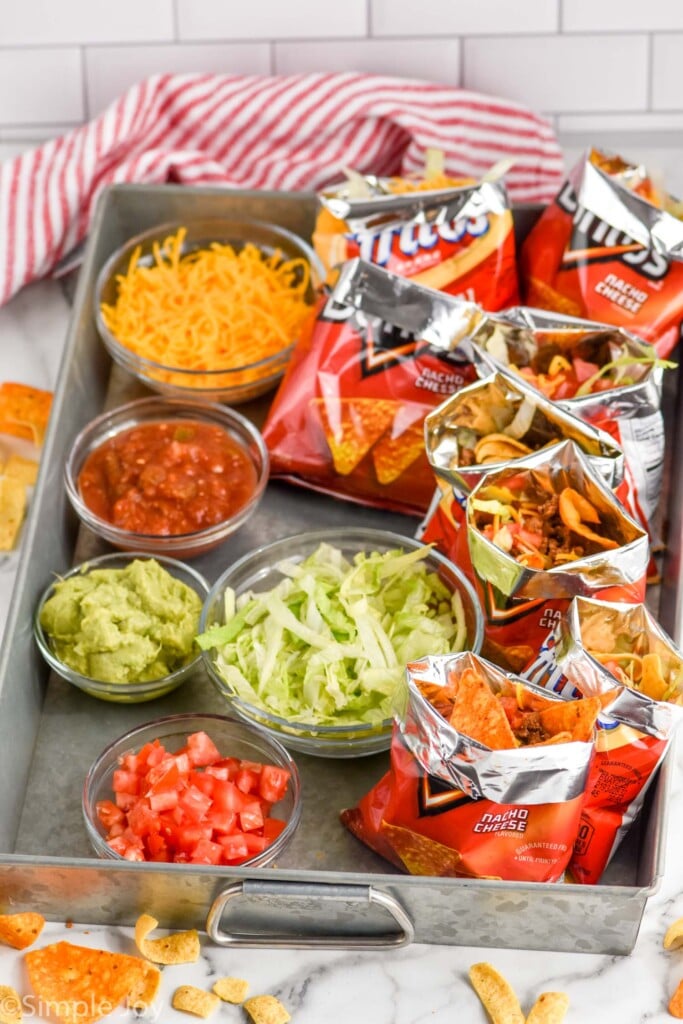 Tray of bowls of Walking Tacos toppings with bags of chips and Walking Tacos sitting beside