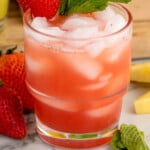Pinterest graphic for Agua Fresca recipe. Picture of strawberry of Agua Fresca garnished with a strawberry and mint leaves. Strawberries and mint leaves beside glass. Text says, "super easy Agua Fresca simplejoy.com."