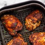 Pinterest graphic for Air Fryer Chicken Thighs recipe. Text says, "Air Fryer Chicken Thighs simplejoy.com." Image shows overhead view of Air Fryer Chicken Thighs in an air fryer basket.