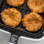 Pinterest graphic for Air Fryer Turkey Burgers recipe. Image shows overhead view of an air fryer basket with Air Fryer Turkey Burgers after cooking. Text says, "Air Fryer Turkey Burgers simplejoy.com."
