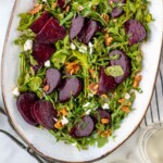 Pinterest graphic for Beet Salad recipe. Platter of Beet Salad garnished with goat cheese and walnuts, with dressing and walnuts beside. Text says, "the best Beet Salad recipe simplejoy.com."