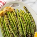 Pinterest graphic for Grilled Asparagus recipe. Text says, "the best Grilled Asparagus simplejoy.com." Image shows a platter of Grilled Asparagus with lemon wedges as garnish.
