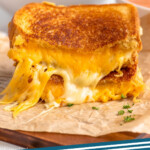 Pinterest graphic for grilled cheese sandwich recipe. Image shows two halves of a grilled cheese sandwich stacked on top of each other with bowls of tomato soup beside. Text says, "grilled cheese simplejoy.com."