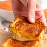 Pinterest graphic for grilled cheese sandwich recipe. Text says, "the best grilled cheese simplejoy.com." Image shows a person's hand pulling apart half of grilled cheese sandwich with tomato soup in the background.