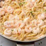Pinterest graphic for Shrimp Alfredo recipe. Image shows a skillet of Shrimp Alfredo recipe with forks for serving. Text says, "super easy Shrimp Alfredo simplejoy.com."
