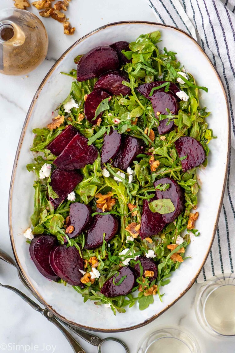 Overhead view of a platter with Beet Salad. Dressing and serving tongs beside.