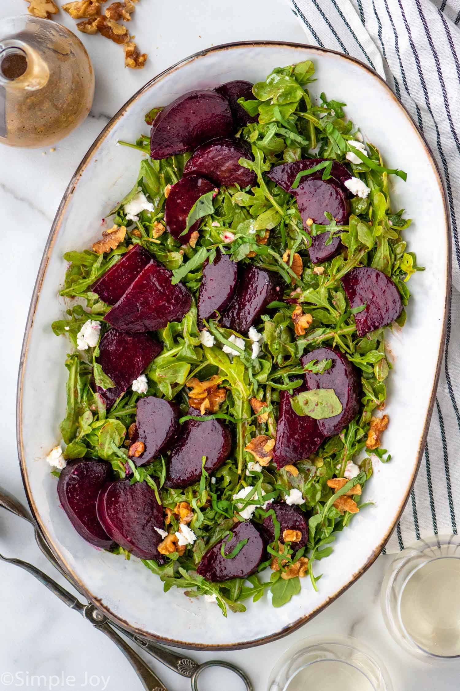 Overhead view of a platter with Beet Salad. Dressing and serving tongs beside.