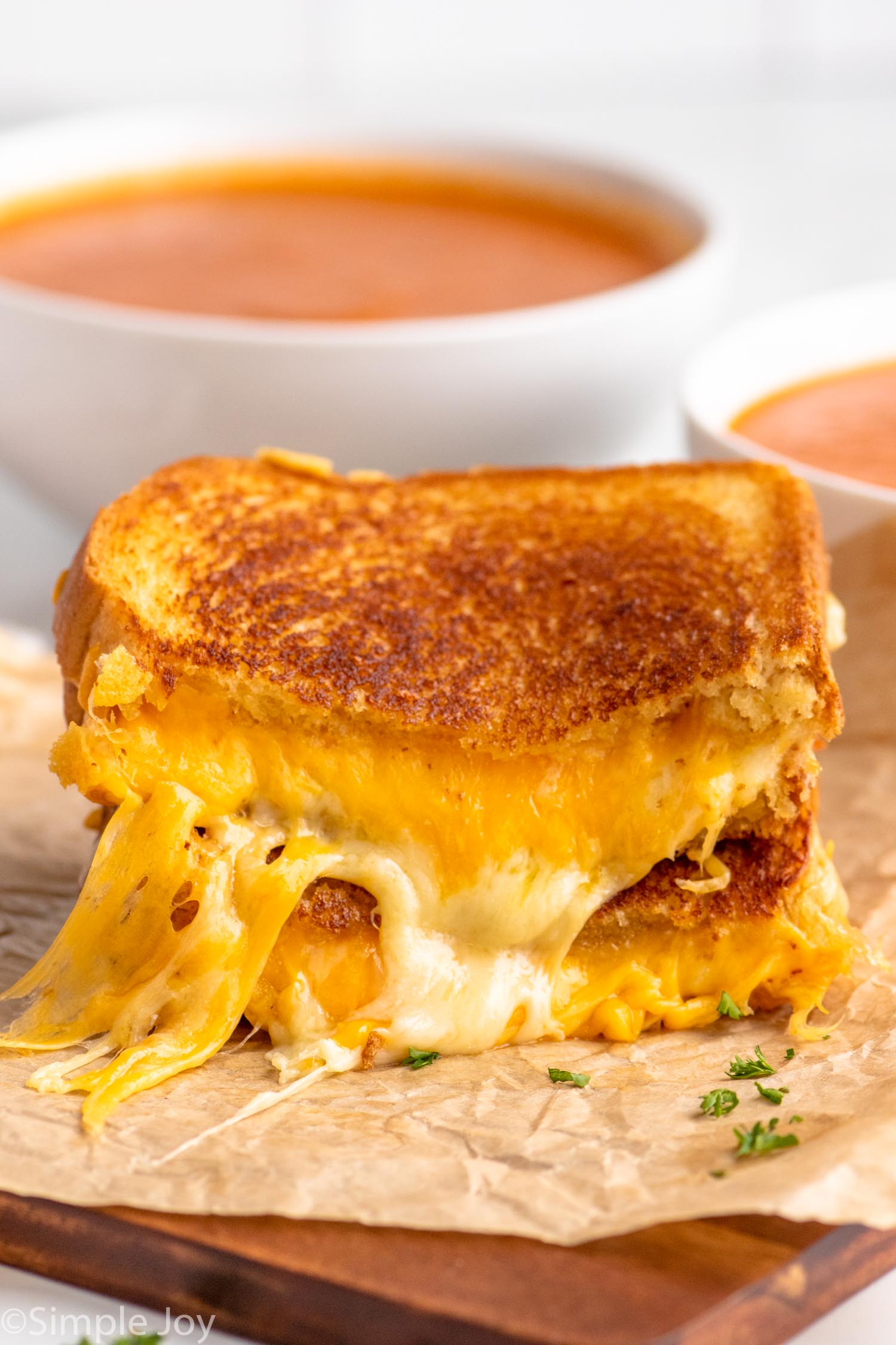 Side view of a grilled cheese sandwich cut in half with the halves stacked on top of each other. Bowls of tomato soup in the background.