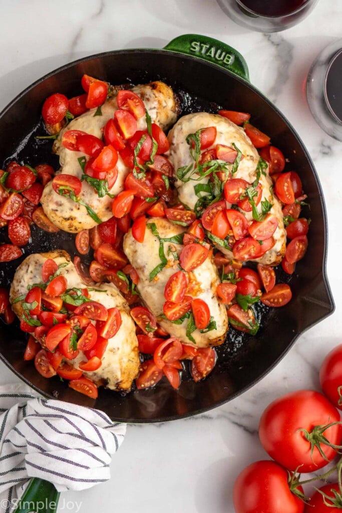 Overhead view of a skillet of Bruschetta Chicken with tomatoes beside.