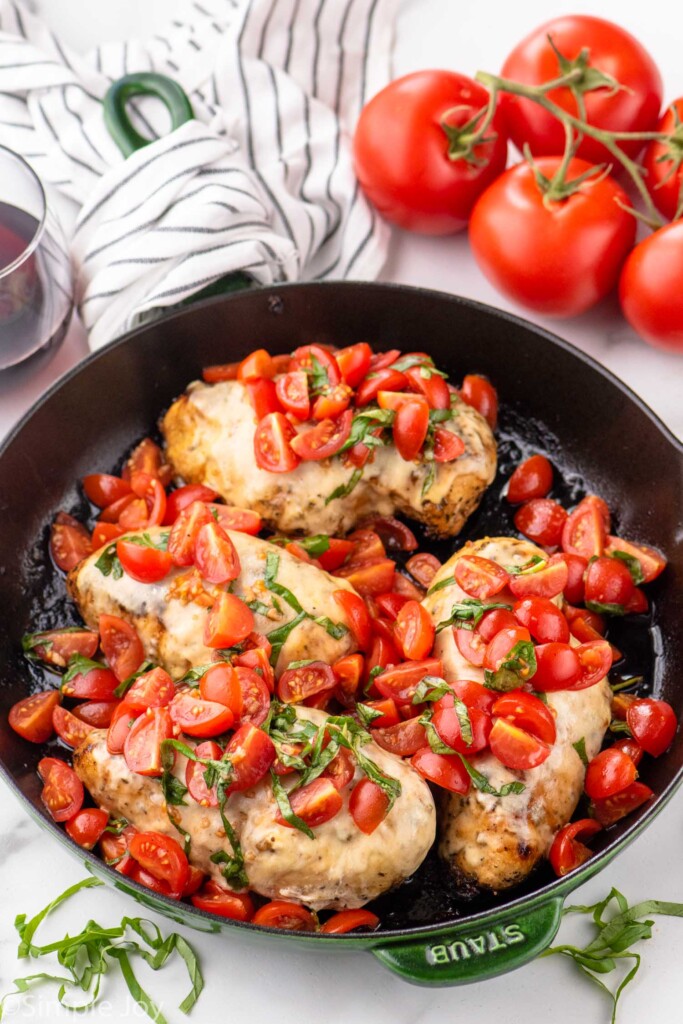 Skillet of Bruschetta Chicken with tomatoes and shredded basil beside.