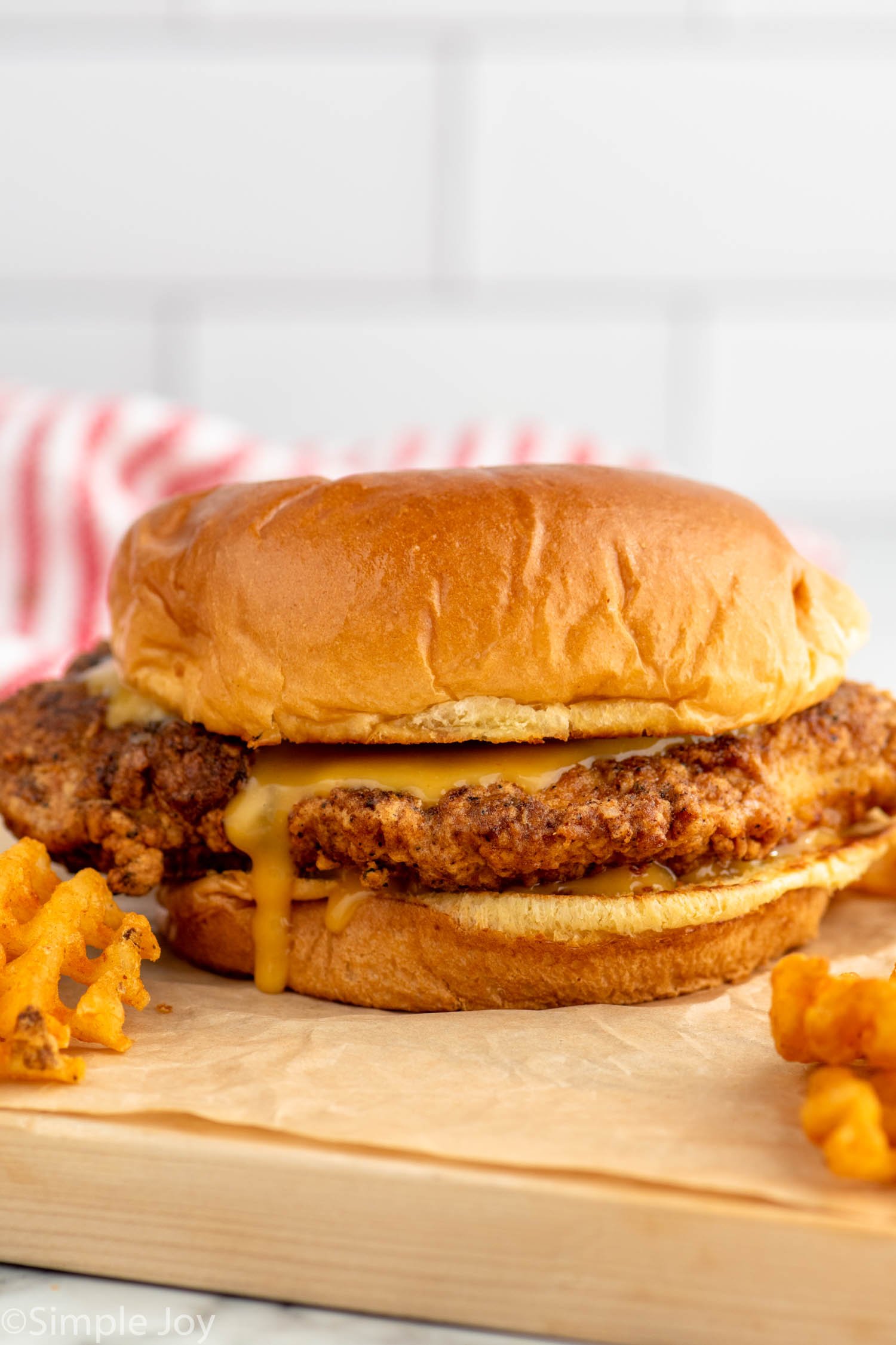 Side view of Chicken Sandwich with pickles, chick fil a sauce on bun with waffle fries beside.