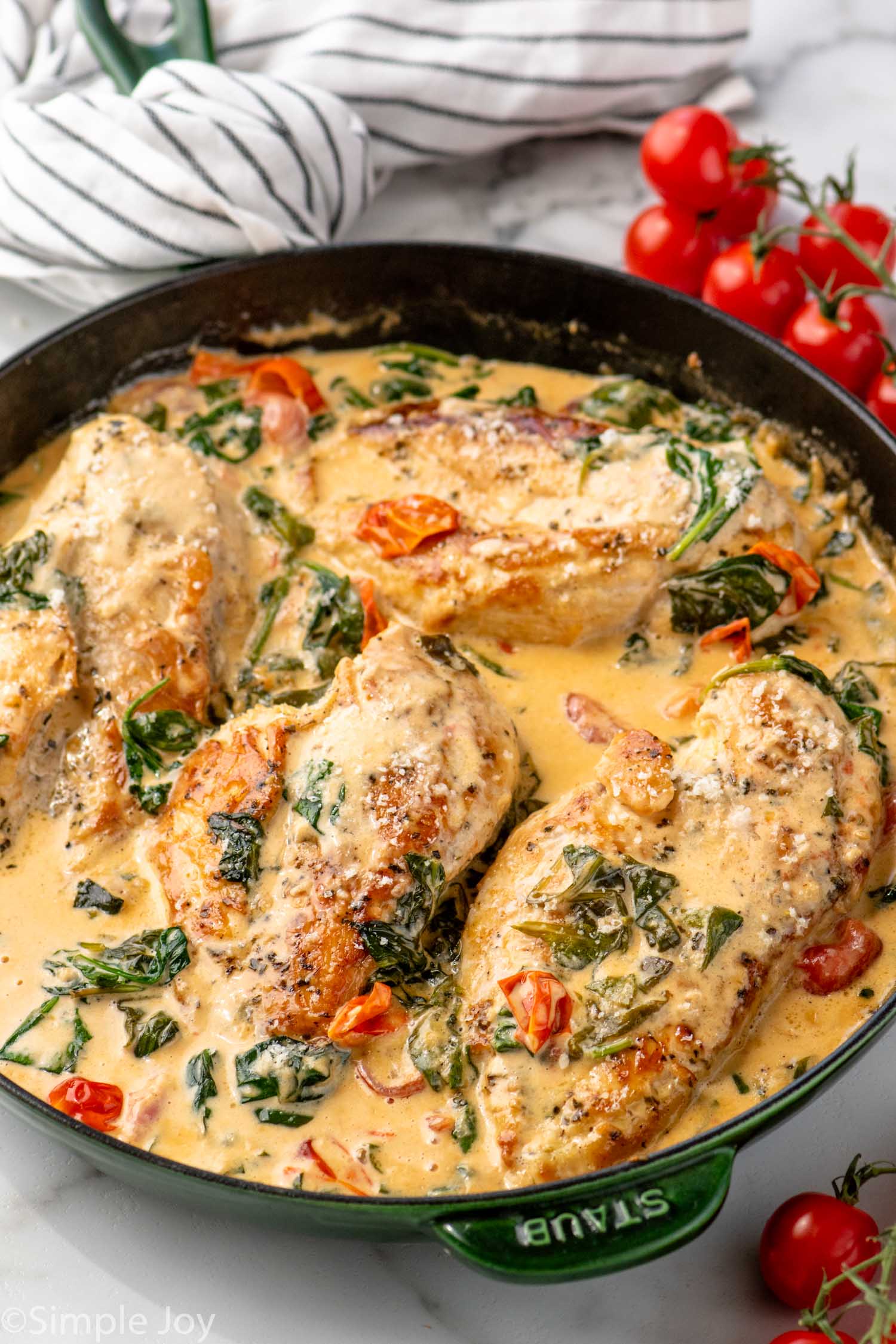 Skillet of Tuscan Chicken with cherry tomatoes beside.
