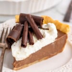 Slice of Chocolate Cream Pie garnished with whipped cream and chocolate shavings served on a plate with a fork.