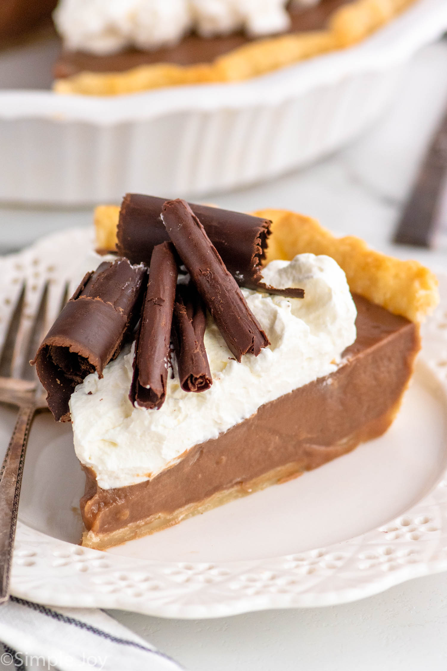 Slice of Chocolate Cream Pie garnished with whipped cream and chocolate shavings served on a plate with a fork.