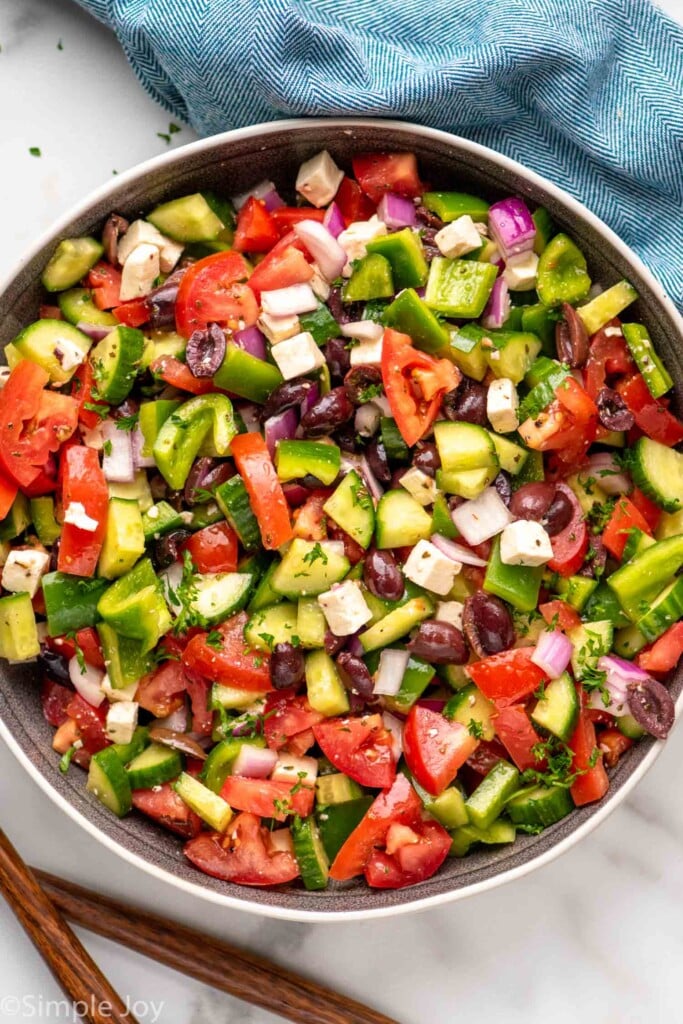Overhead view of a bowl of Greek Salad garnished with dressing, feta cheese, and oregano.