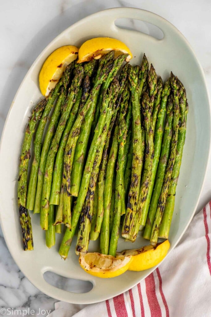 Overhead view of a platter of Grilled Asparagus garnished with lemon wedges