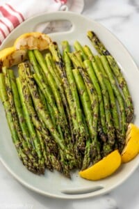 Platter of Grilled Asparagus garnished with lemon wedges.