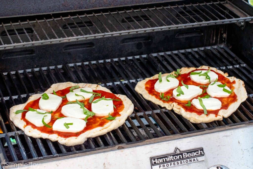 Two pizzas with cheese and basil on grill for Grilled Pizza recipe.