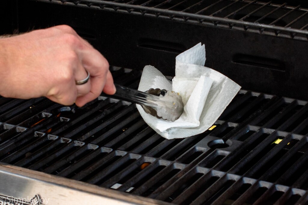 Person's hand holding tongs to prepare grill for Grilled Pizza recipe.