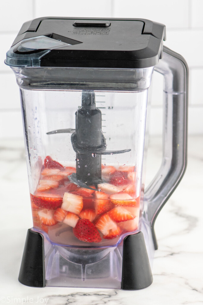 Side view of blender with strawberries and ingredients for Agua Fresca recipe.