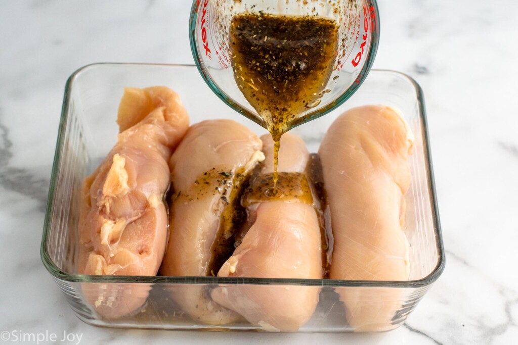 Measuring cup of marinade being poured over container of raw chicken breasts for Bruschetta Chicken recipe.