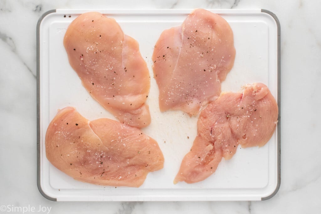 Overhead view of seasoned raw chicken breasts on cutting board for Chicken Sandwich recipe.