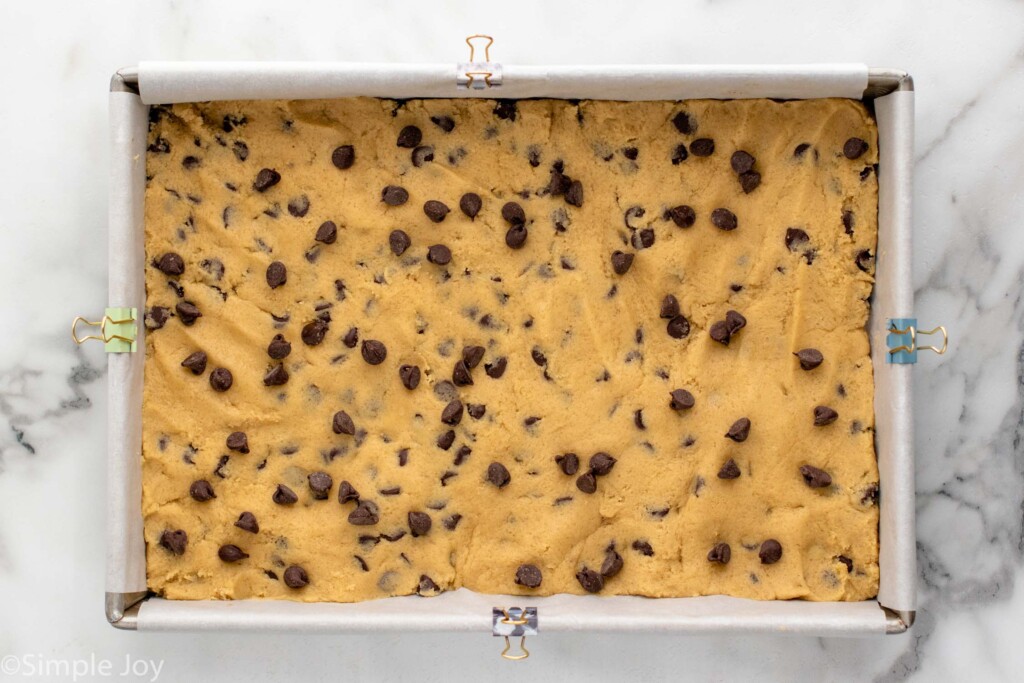 overhead of Chocolate Chip Cookie Bars dough pressed into a baking pan lined with parchment paper