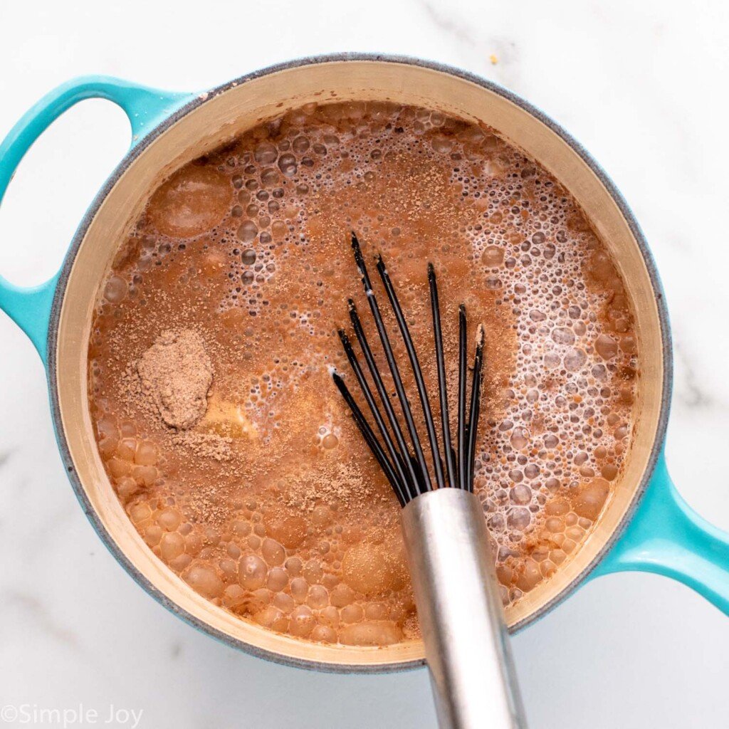 Overhead view of a sauce pan of ingredients and whisk for stirring for Chocolate Cream Pie recipe.