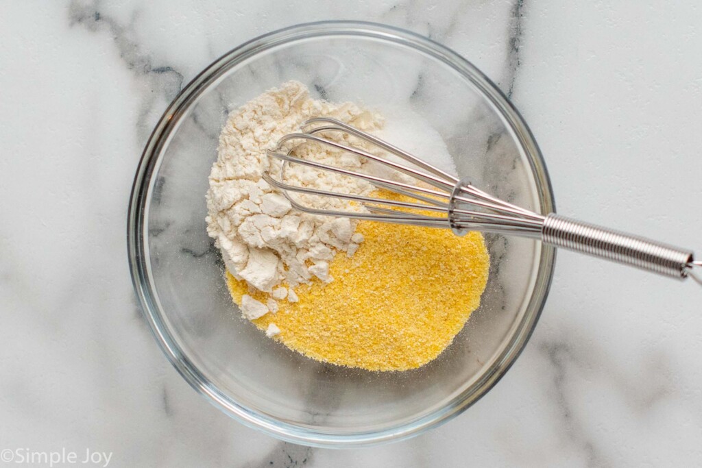 Overhead view of dry ingredients in a mixing bowl with a whisk for Chess Pie recipe.