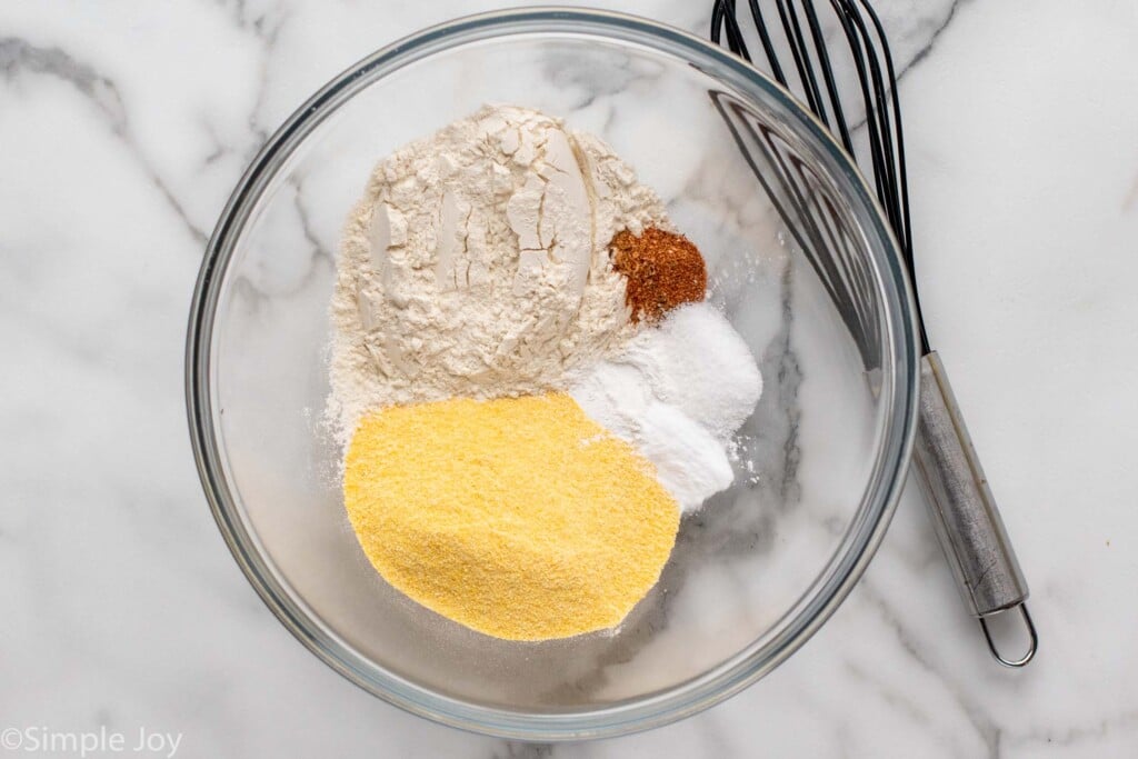 Overhead view of a mixing bowl of dry ingredients for Hush Puppies recipe. Whisk for mixing beside.
