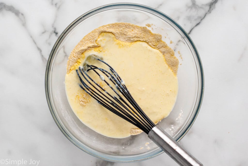 Overhead view of a mixing bowl of ingredients for Hush Puppies recipe with a whisk for mixing.