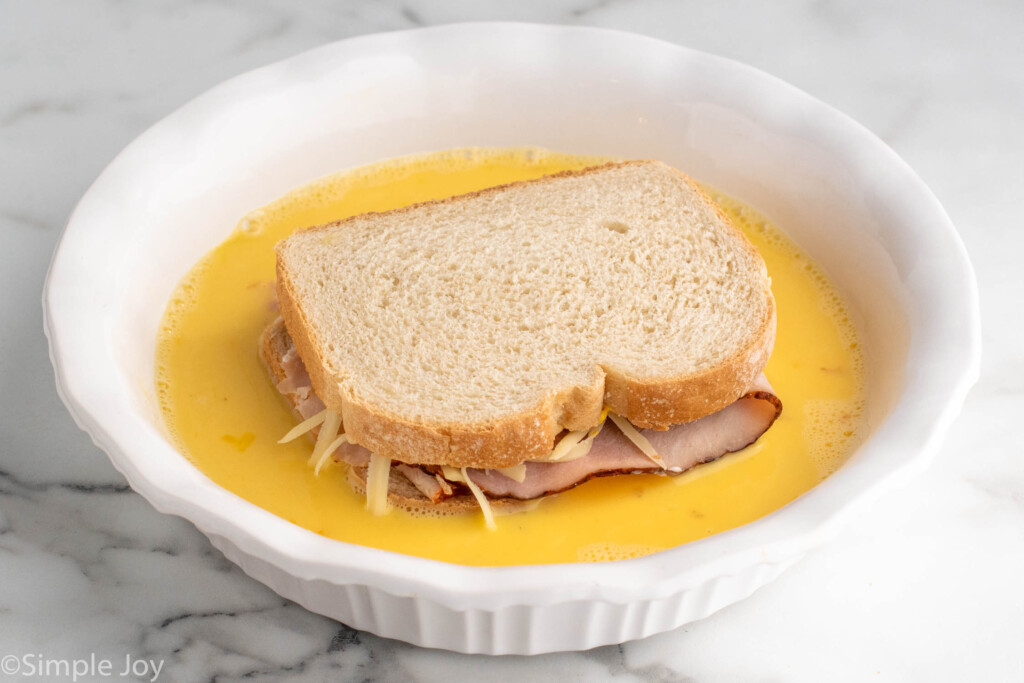 monte cristo sandwich being dipped in an egg batter