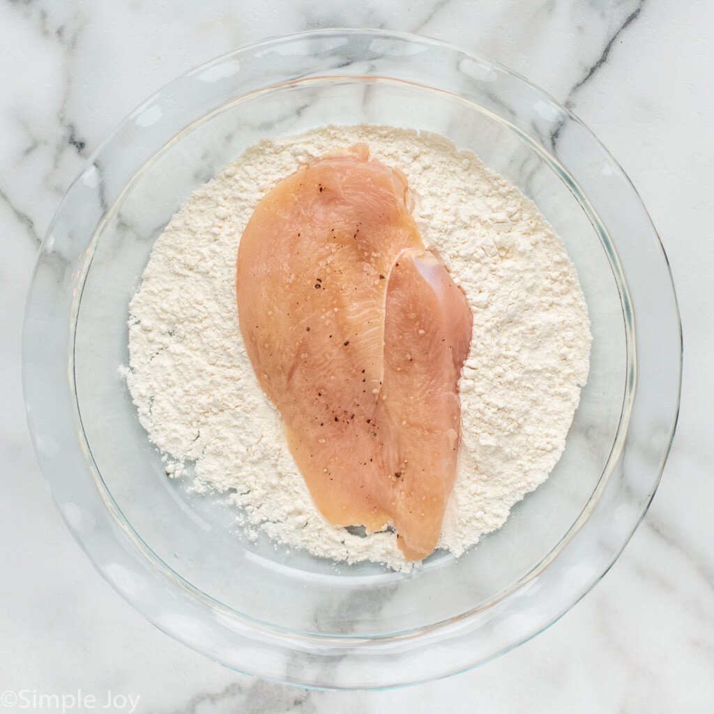 overhead of chicken in a bowl of flour to make Parmesan Crusted Chicken