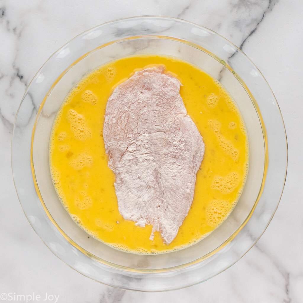 overhead of a piece of chicken in a bowl of eggs to make Parmesan Crusted Chicken